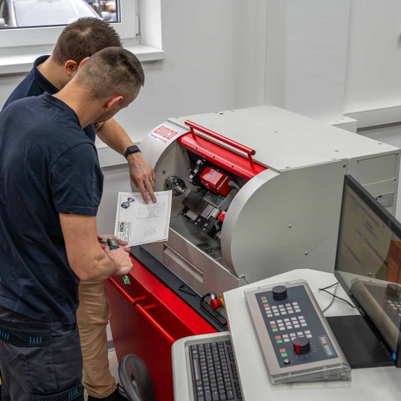 Lektor a študent počas výučby na CNC sústruhu v Akadémii CNC, konzultujú technický výkres