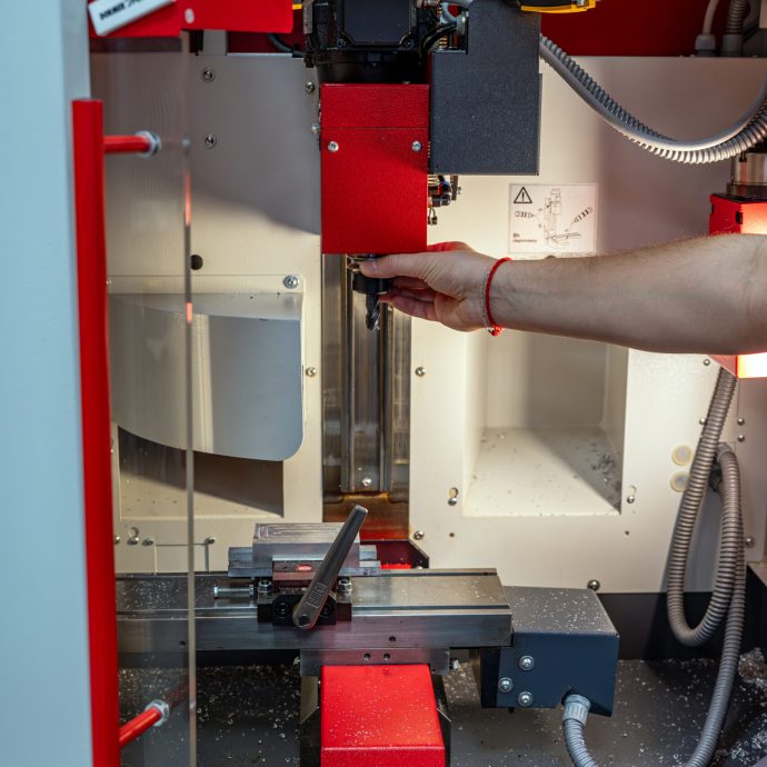 Praktický nácvik výmeny nástroja Ruka študenta vkladá frézovací nástroj do vretena CNC stroja EMCO Concept Mill 55