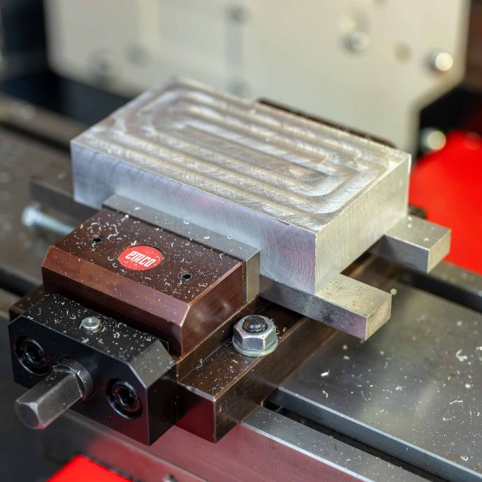 Reálny výsledok z reálneho CNC stroja Detail obrobeného hliníkového dielu upnutého vo zveráku počas výučby CNC frézovania